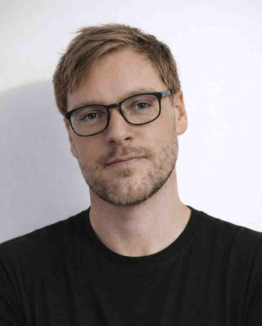 Professional headshot of the architectural designer and founder of 30 Create, featuring a man with glasses and a black shirt against a minimalist white background.